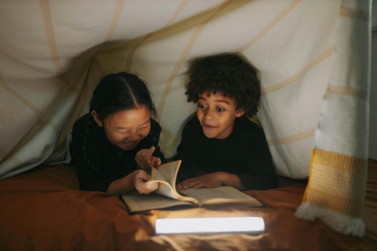 children reading a book under a blanket